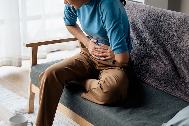 Woman sitting and holding her stomach, experiencing pelvic pain associated with endometriosis.