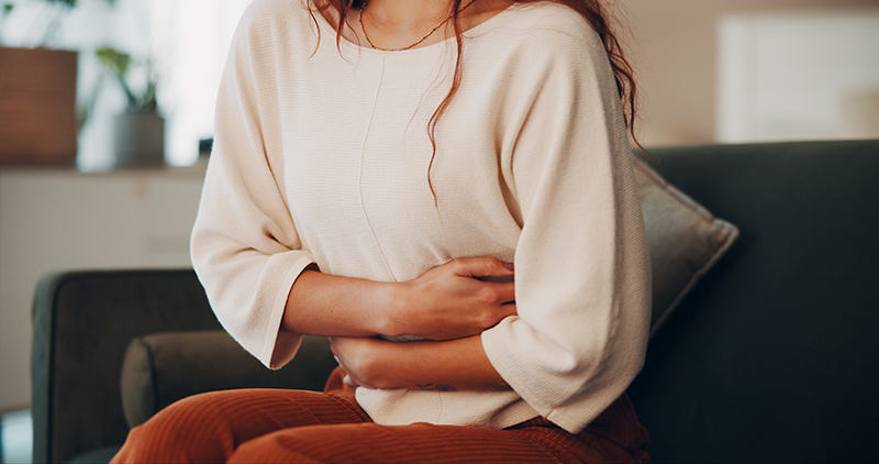 Woman holding her lower abdomen in discomfort at home, illustrating symptoms of endometriosis and pelvic pain.